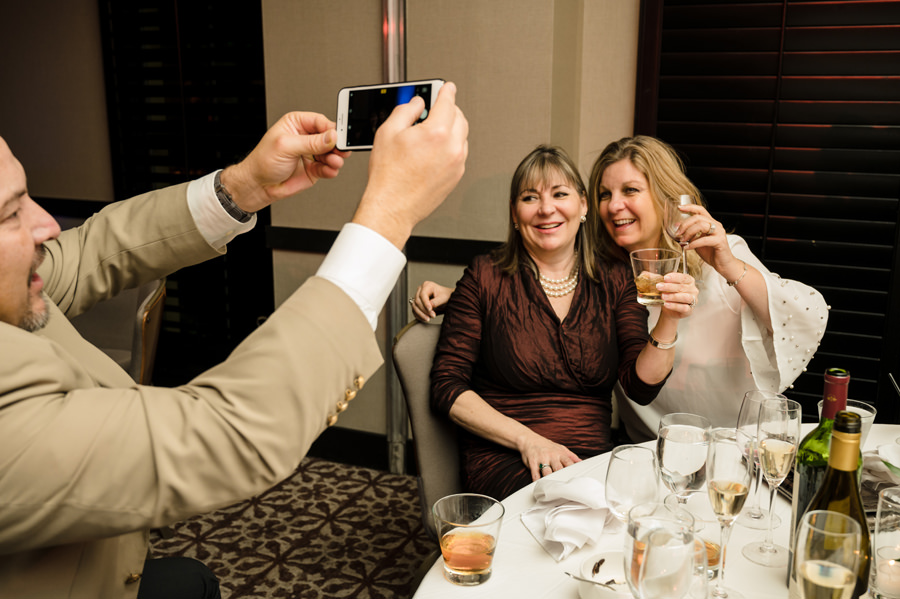 An image of a man snapping picture of his 2 lady friends using the cell phone.