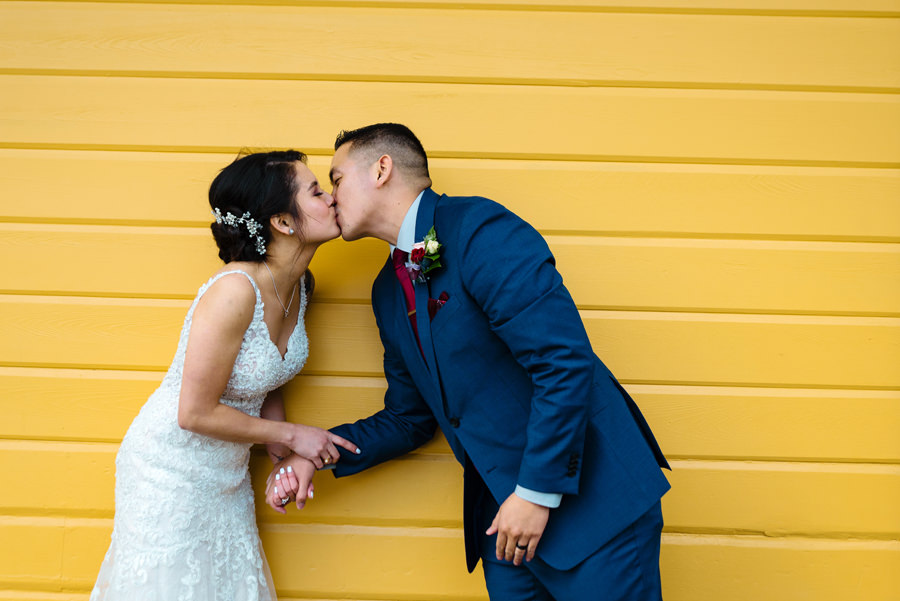 A photo of newly wed kissing in front of a yellow wall