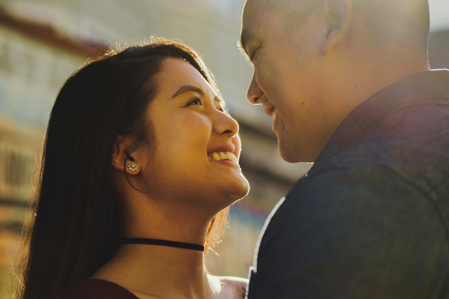 An image of an engaged couple smiling as they stand face to face illuminated by a beautiful natural daylight