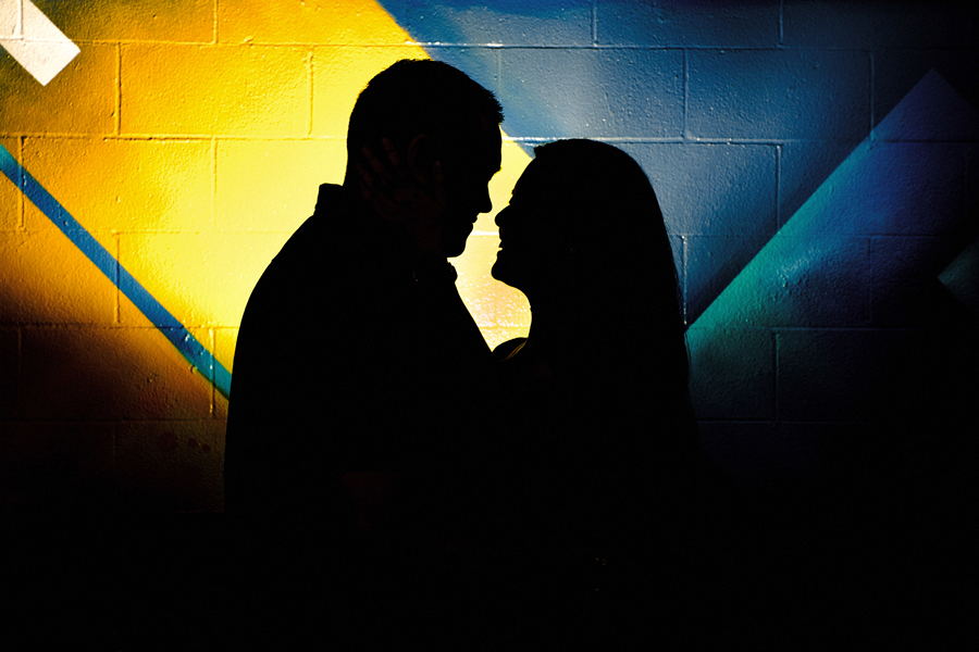 A great silhouette image of a couple embraced in front of painted wall