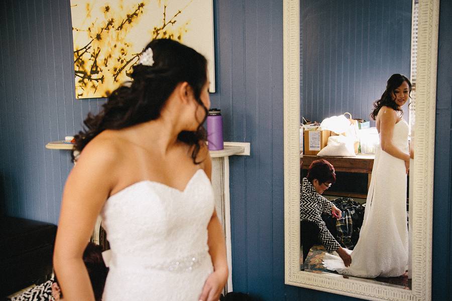 Bride looking at the mirrow while her aunt straightening her Wedding dress train