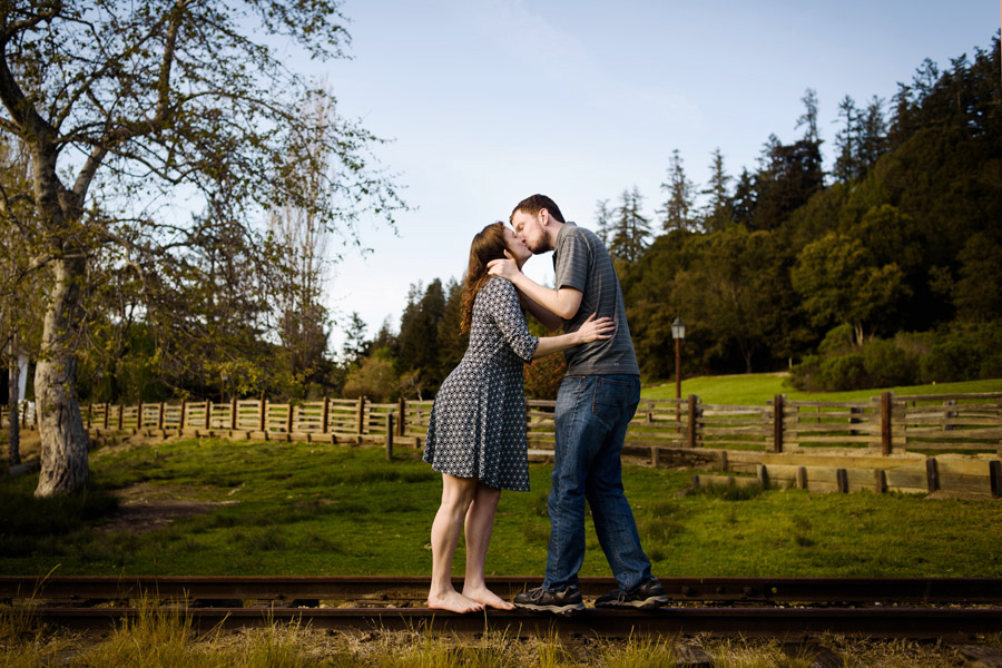 A cute picture of a couple kissing while standing on the rail road track