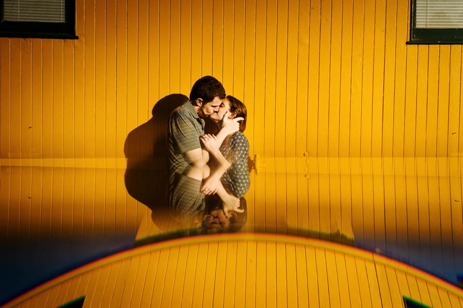 A couple kissing in front of a yellow mustart wooden wall