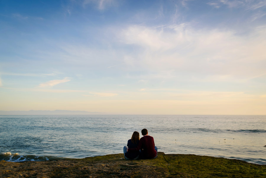 A couple sits on the rock while watching the Pacific Ocean