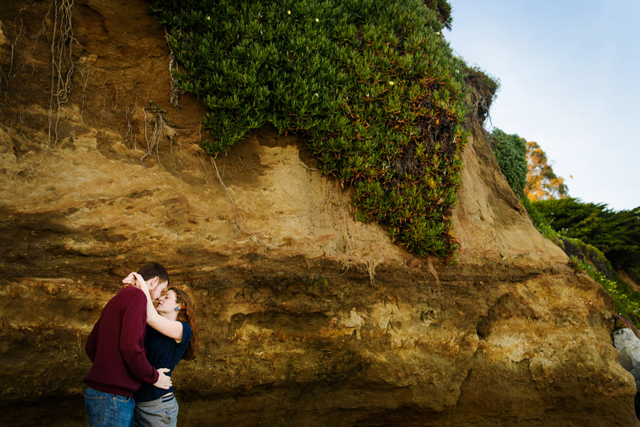 A couple showing affection next a beach boulder