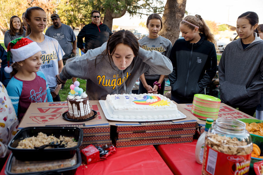 A birthday girl blowing the birthday candle surrounded by her friends and family.