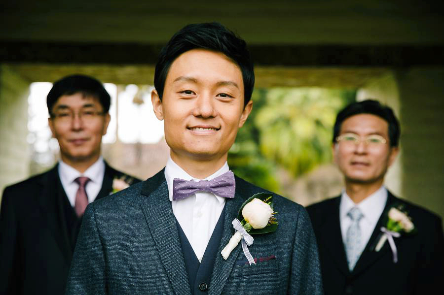 The groom smiles while his father and father in law looks on the background