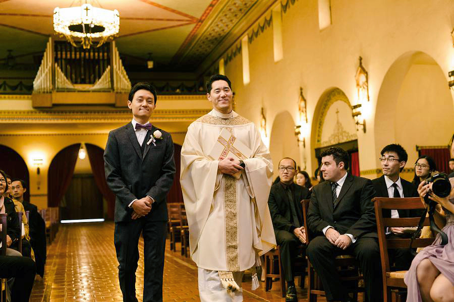 Groom walks the aisle with the priest to start the ceremony at Santa Clara University Mission Church