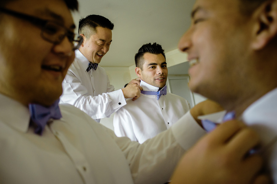 Groomsmen helping each other putting up their lilac color bowtie