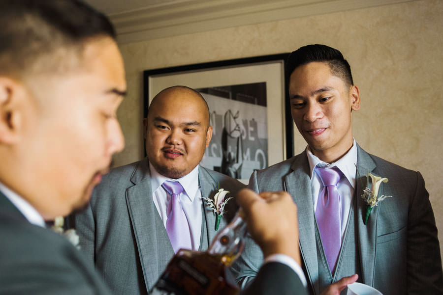 A groom kissing an unopened bottle of whiskey before sharing it with his groomsmen