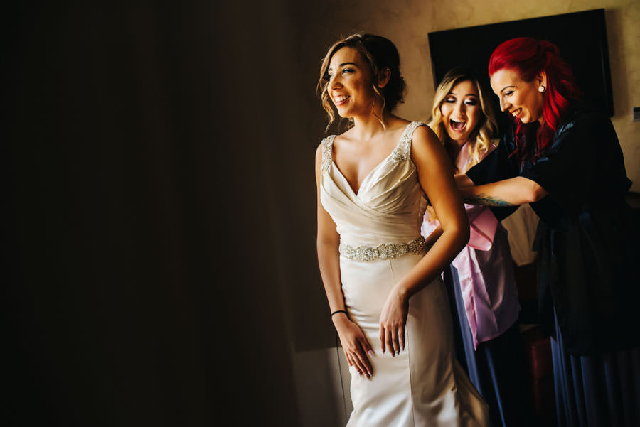 Bridesmaids help zipping up the back zipper of a bride's wedding dress