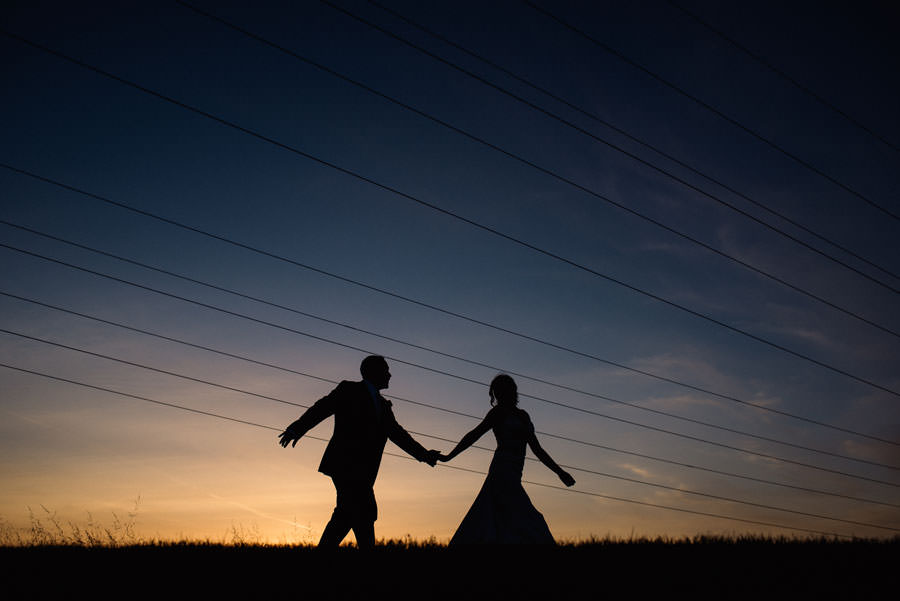 A beautiful silhouette of bride and groom walking across the field with the sunset sky in the background