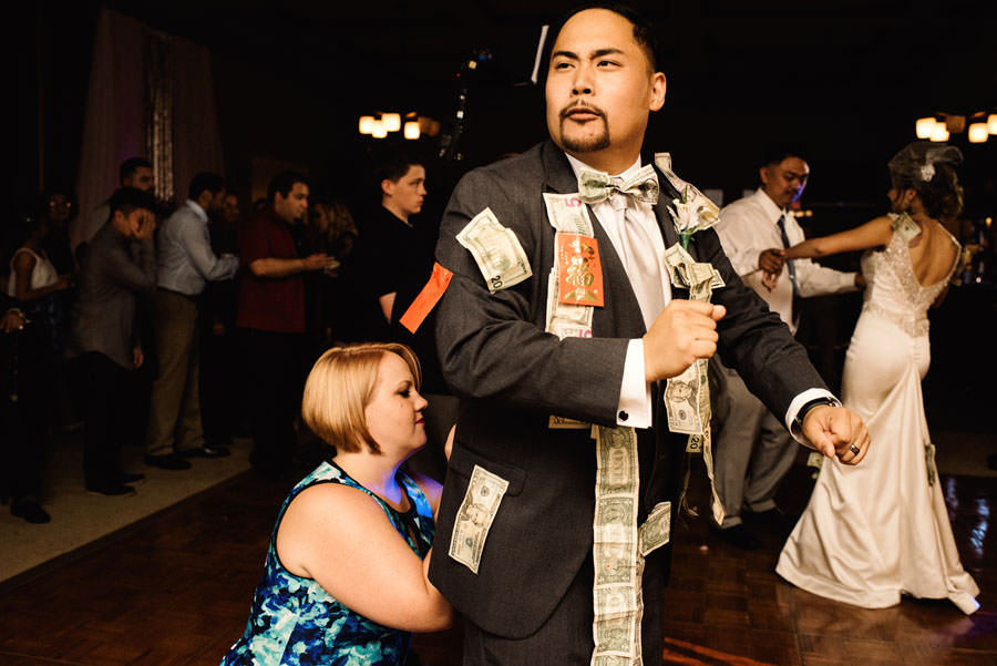 Groom making faces while a guest pinning money on his suit during the money dance