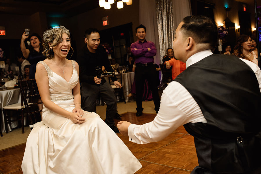 A bride laughs while looking towards his kneeling groom
